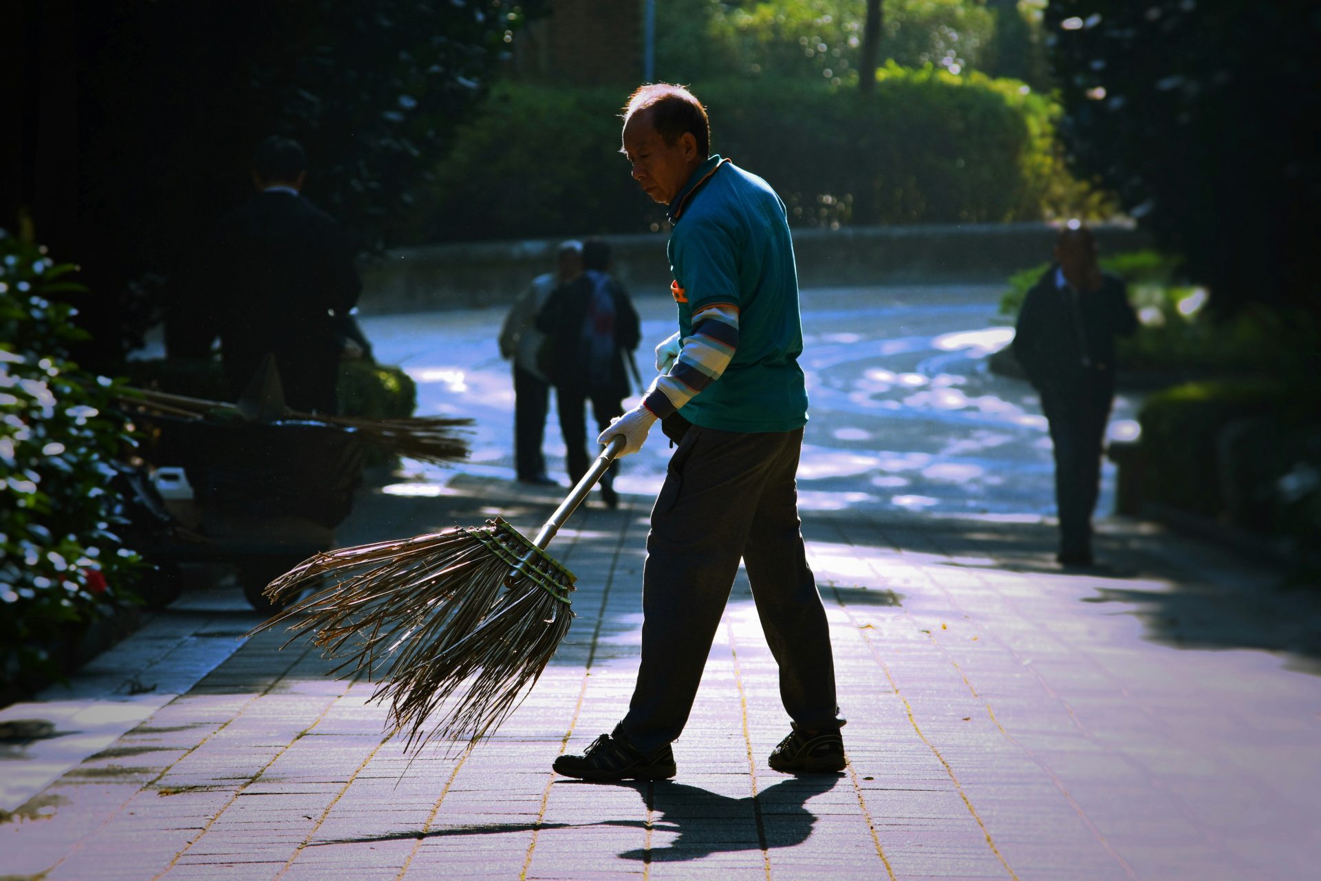 Worker sweeping a pathway with a large broom.