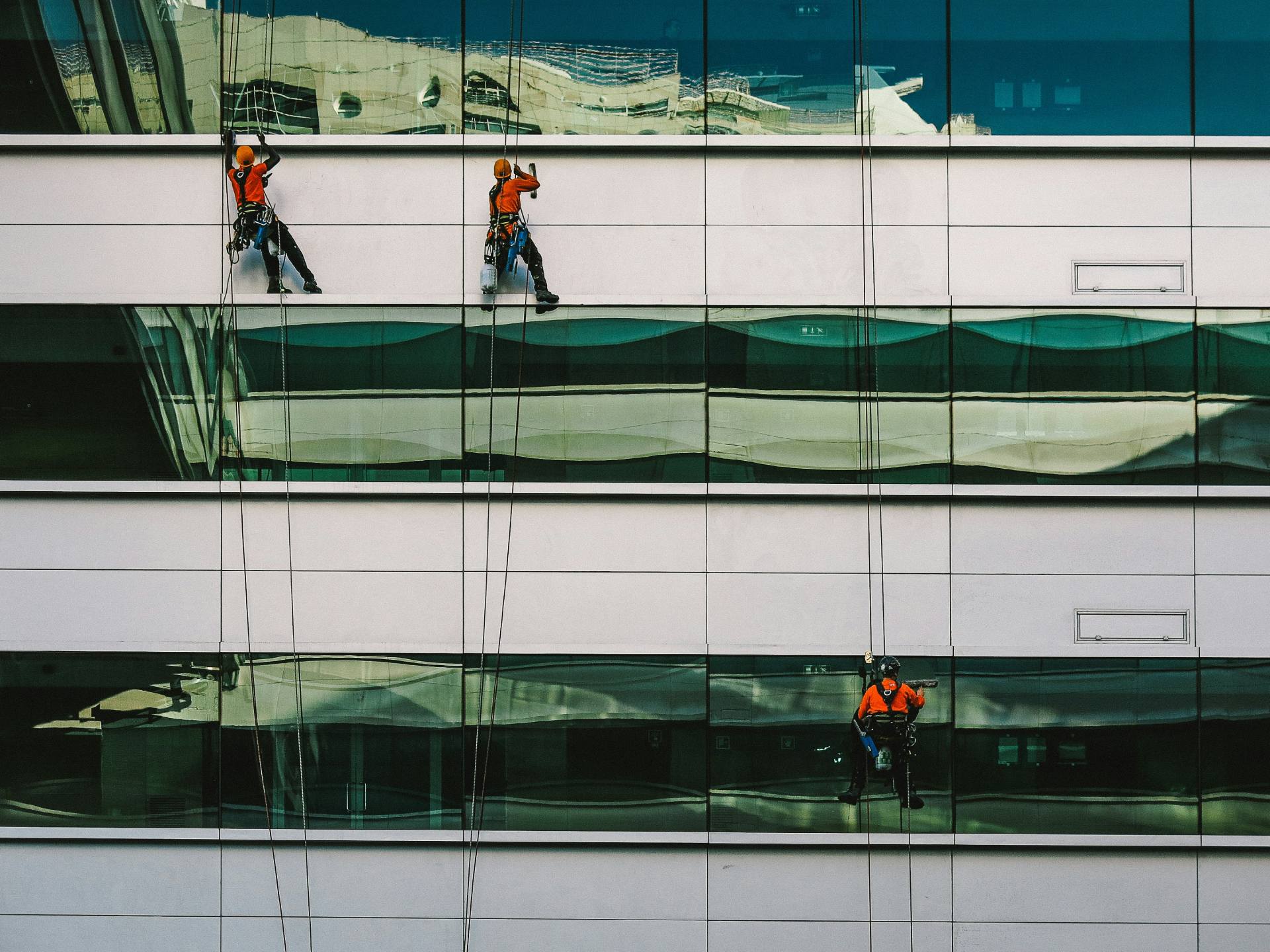 Three workers cleaning windows on a tall building.