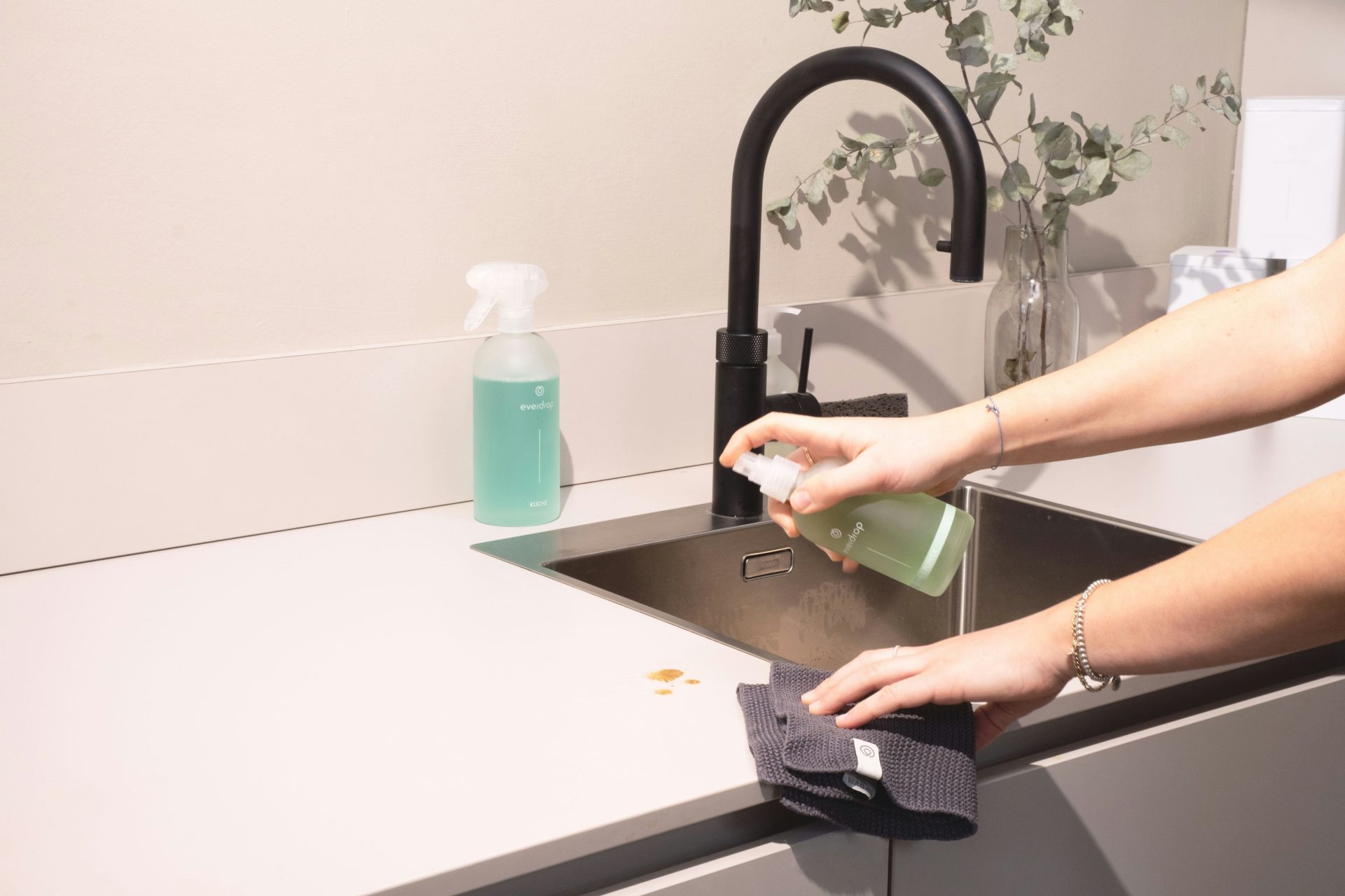 Person cleaning a kitchen counter with spray and cloth.