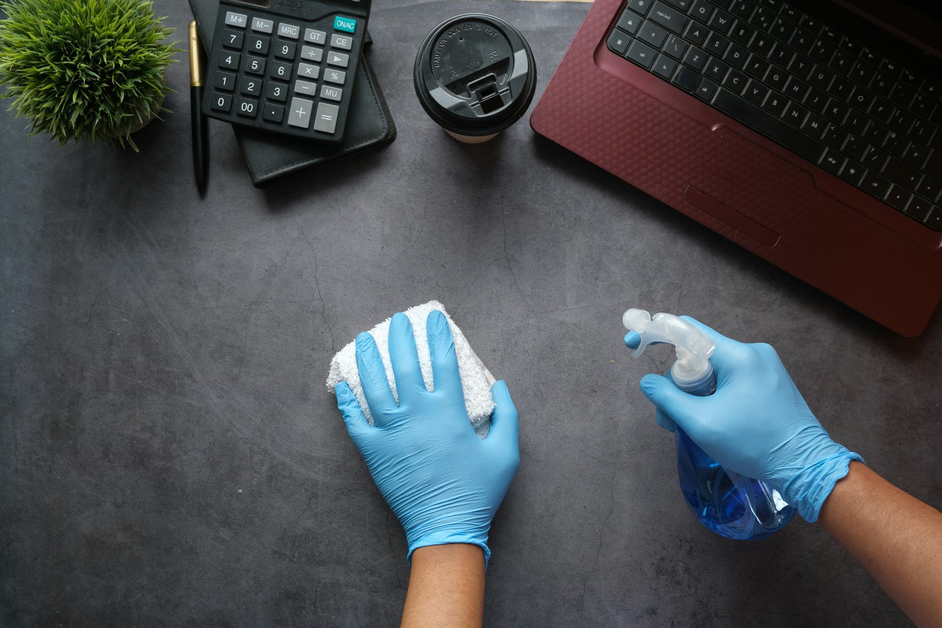 Person cleaning a desk with gloves and a spray bottle