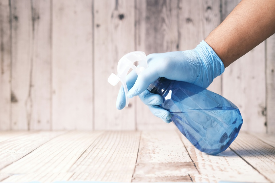 Hand spraying cleaner on a wooden surface with blue gloves.