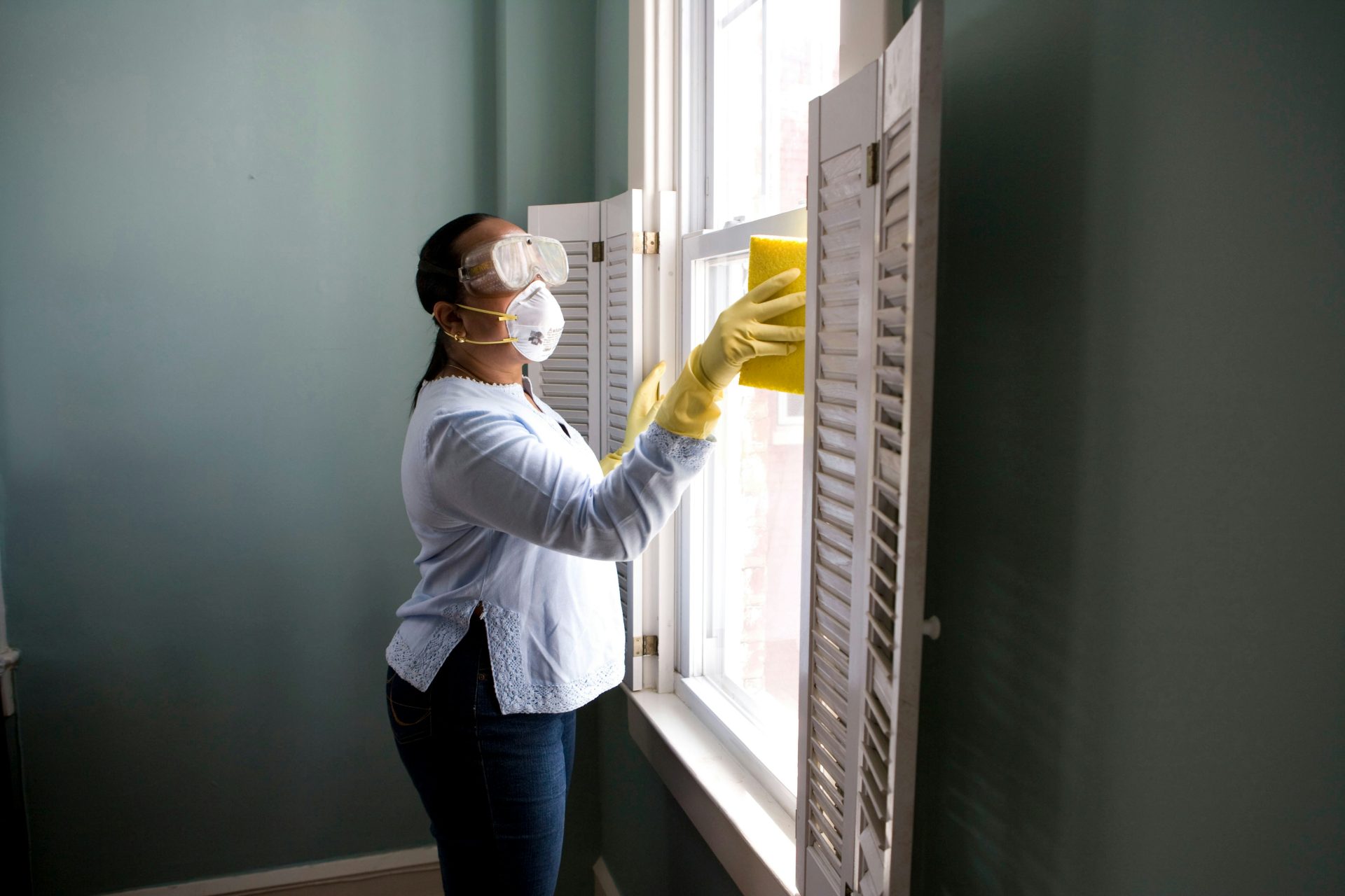 Person wearing goggles and gloves cleaning a window.